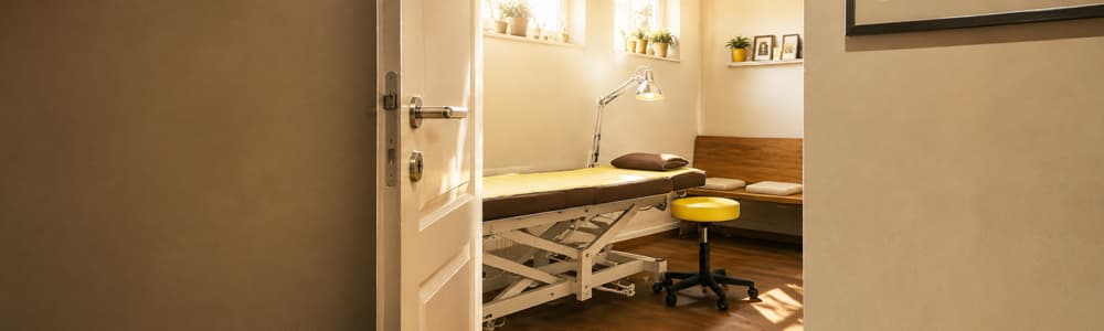 Geöffnete Praxistür mit Blick auf Behandlungsliege im Therapiezentrum Westfalen